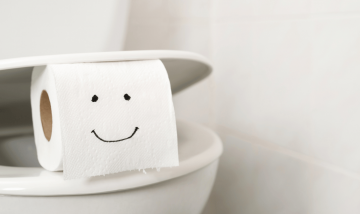roll of toilet paper with smiley face balanced on toilet