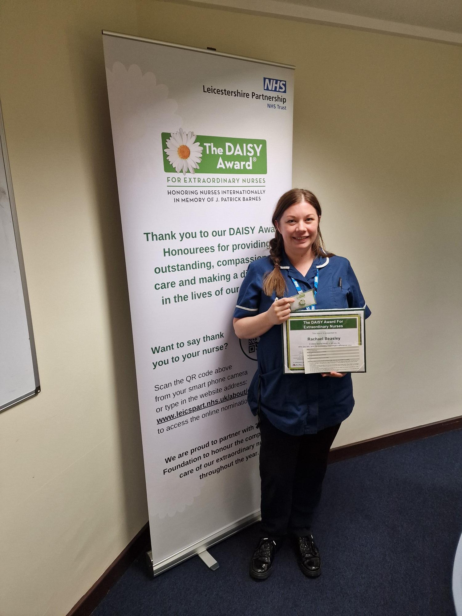 Photo of Rachael Beasley, smiling in her uniform, and holding DAISY Award certificate and pin badge