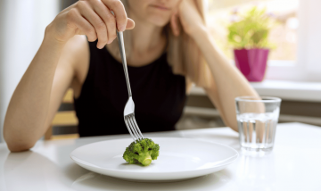 girl holding fork with a plate containing one piece of broccoli