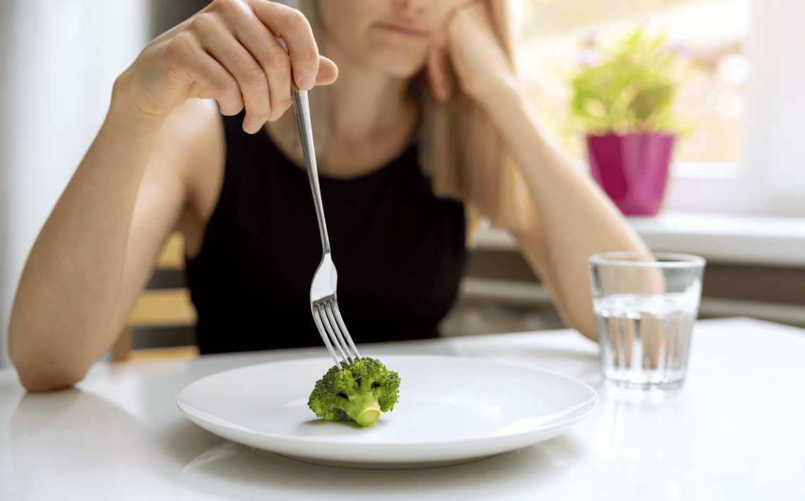 girl holding fork with a plate containing one piece of broccoli